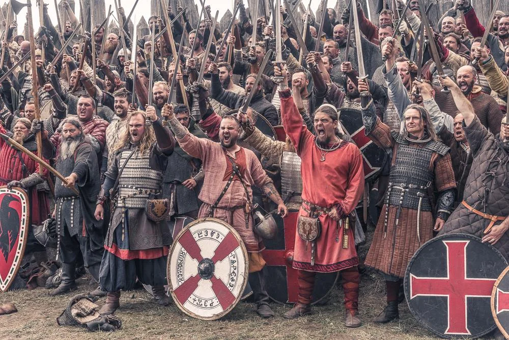 Grupa wikińskich wojowników z uniesionymi rękami w rekonstrukcji historycznej